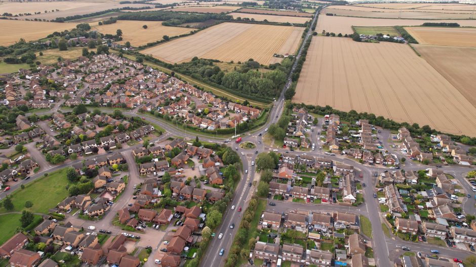 An aerial view of a residential street in Field End Road, Eastcote, showing a row of terraced houses with small, well-maintained gardens at the back. Each garden features lush green lawns, flower beds